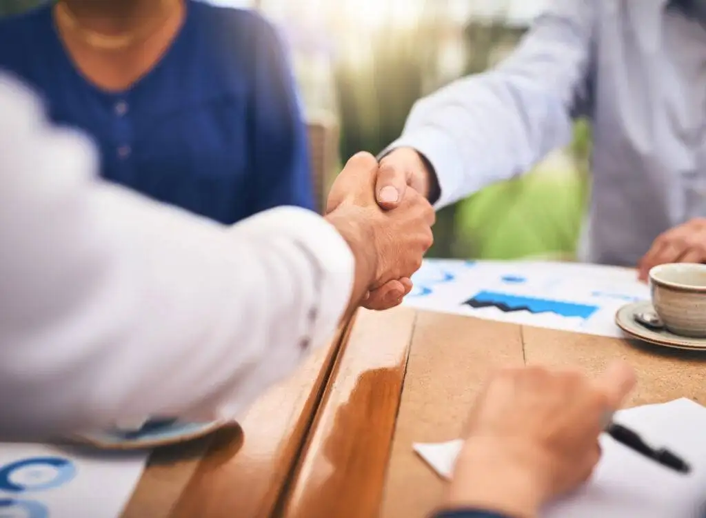 Business people shaking hands in a coffee shop during a teamwork and onboarding meeting.